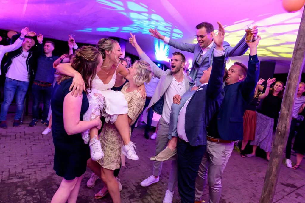 Bruid en bruidegom worden door hun gasten op de schouders getild op de dansvloer