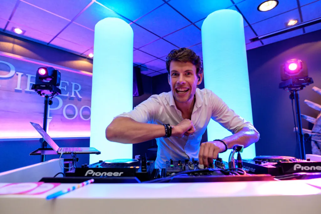 DJ Lars lacht achter de draaitafels bij Pieter Poot, voor blauw en paars verlichte zuilen