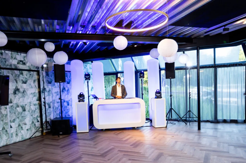 Witte DJ-booth met verlichte zuilen en witte lampionnen in de lichte feestzaal van Villa Kalkoven