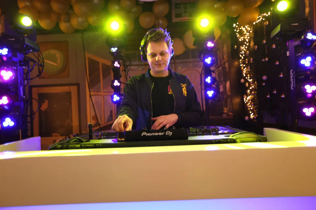 DJ Sipke draait achter een wit verlichte DJ-booth met gele spots en paarse lichtzuilen