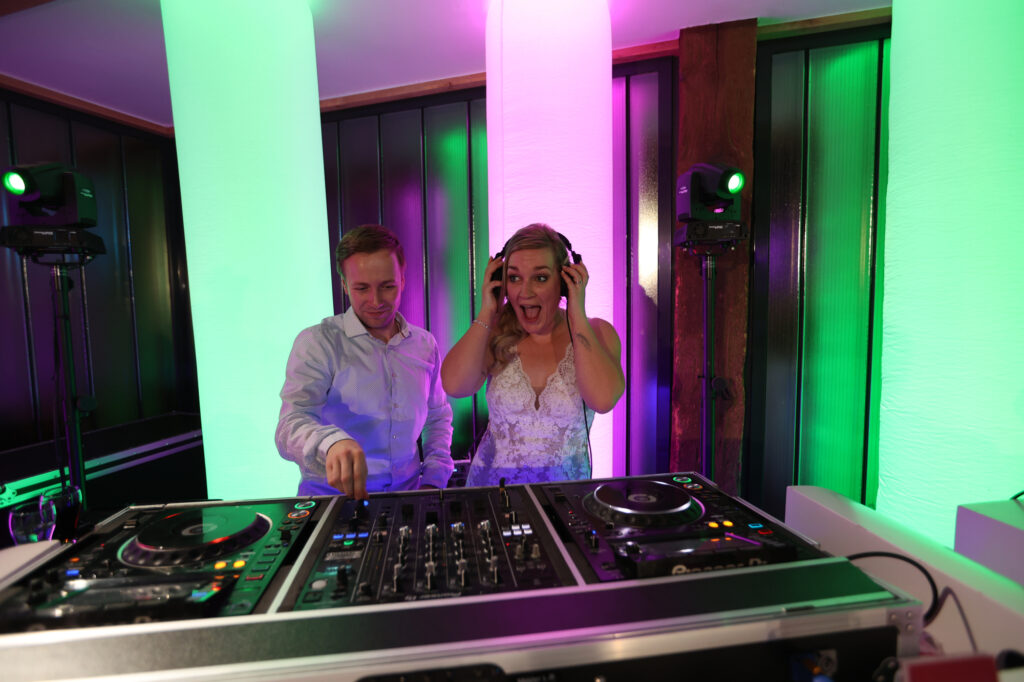 DJ Wiebe en de bruid samen achter de DJ-booth, zij met koptelefoon op, in groen en roze licht