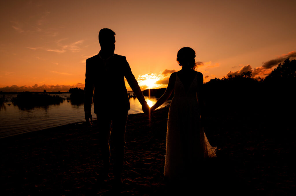 Bruidspaar hand in hand bij zonsondergang aan het water bij Paviljoen de Leyen
