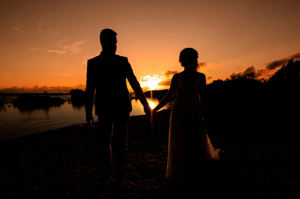 Bruidspaar hand in hand bij zonsondergang aan het water bij Paviljoen de Leyen