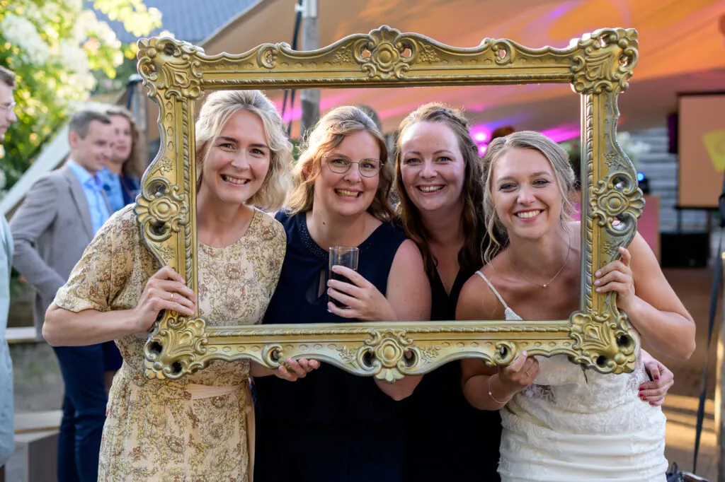 Bruid en vriendinnen poseren met een gouden fotolijst