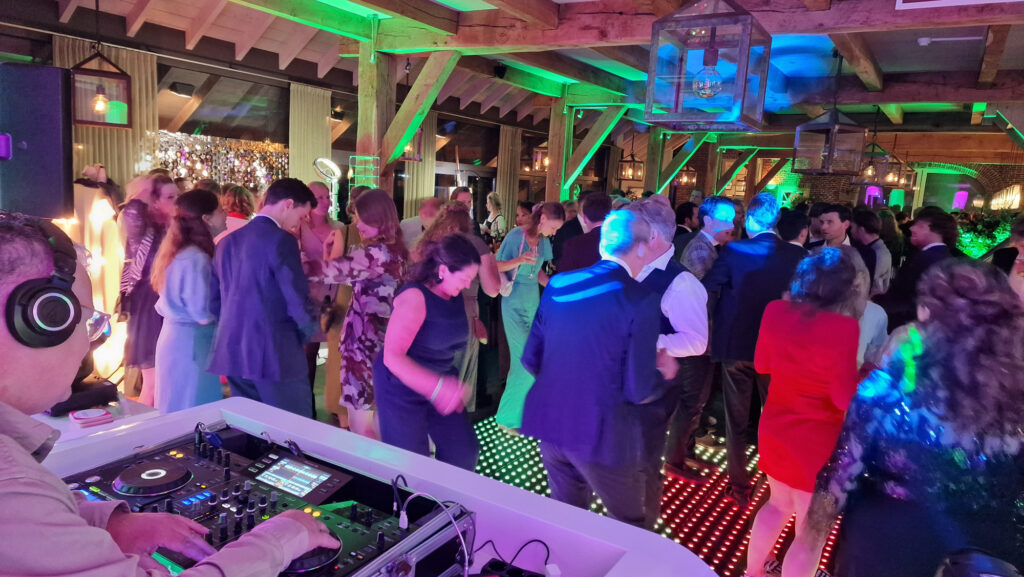 DJ met koptelefoon achter de draaitafels, met dansende gasten op een verlichte LED-dansvloer