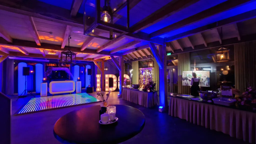 Feestzaal van De Havixhorst met blauw verlichte houten balken, een verlichte dansvloer en de DJ-booth