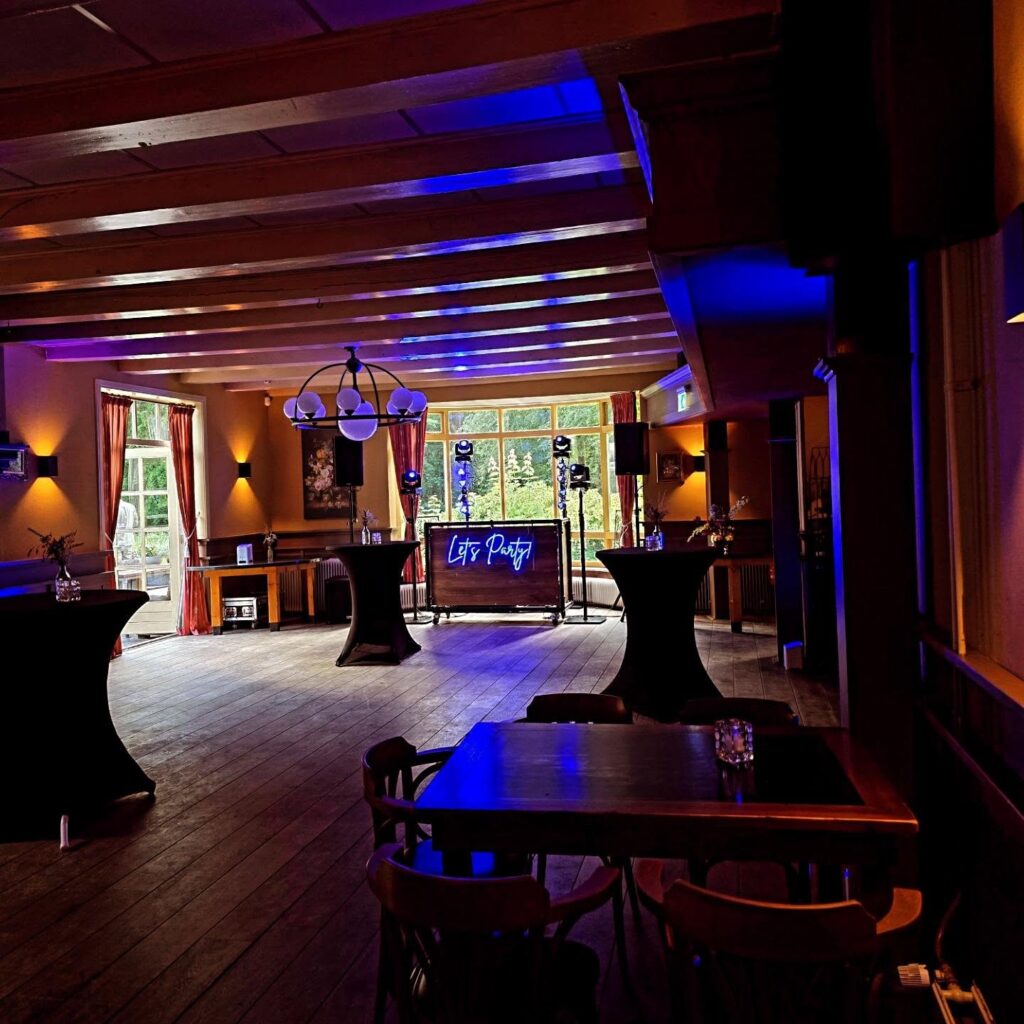 Industriële DJ-booth met Let’s Party-neonbord in de feestzaal van Landgoed Stania State, met blauwe sfeerverlichting