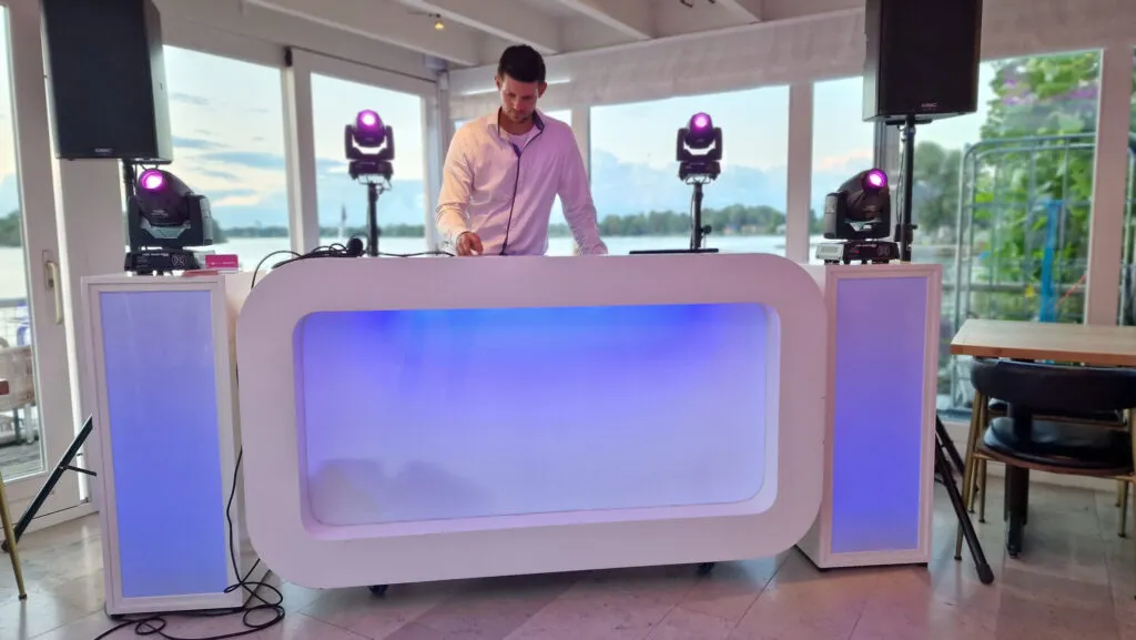 DJ achter de witte DJ-booth met verlichte zuilen en moving heads in De Paalkoepel