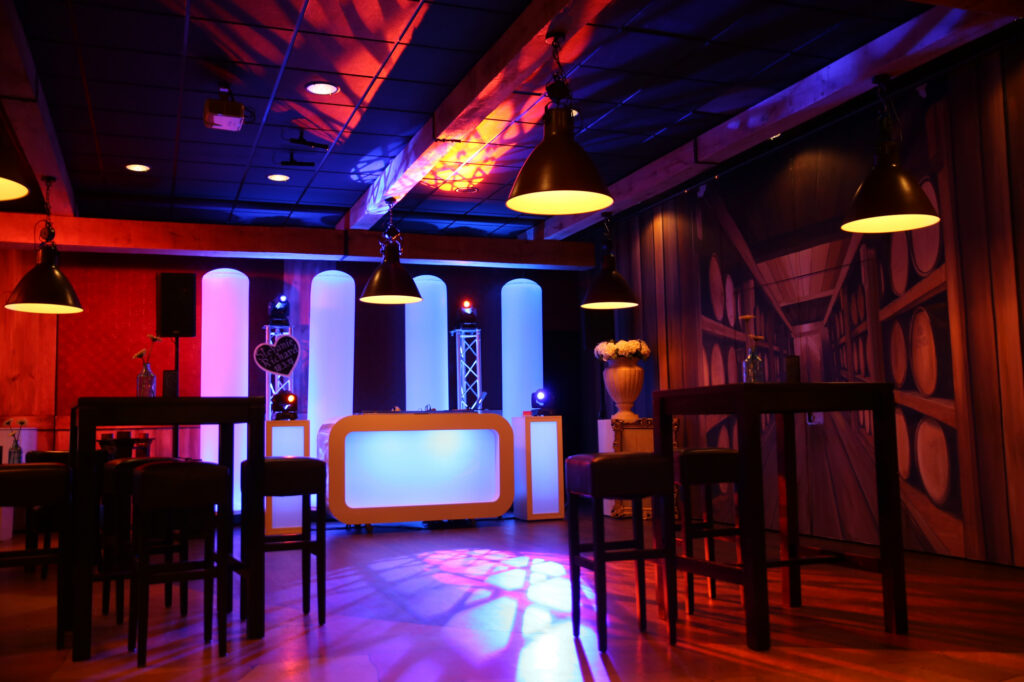 Witte DJ-booth met lichtzuilen op het podium van Pieter Poot, met rood en blauw sfeerlicht