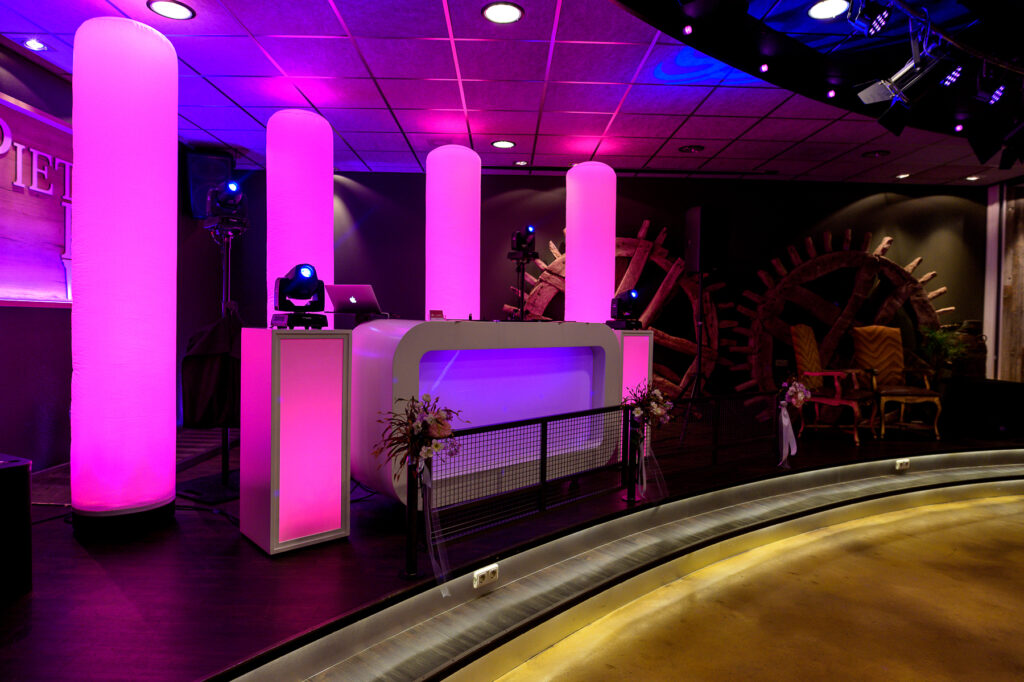 Podium met witte DJ-booth en roze verlichte zuilen in de feestzaal van Pieter Poot