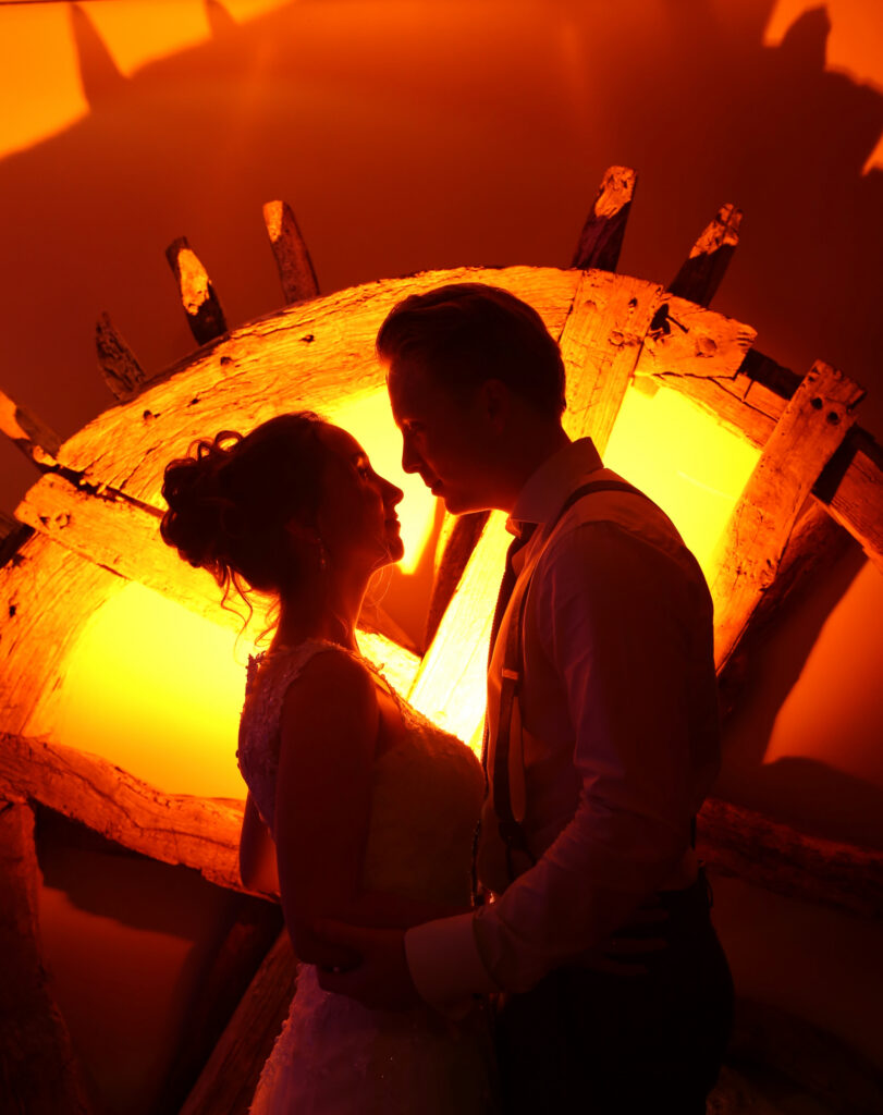 Silhouet van het bruidspaar voor een warm verlichte, ronde doorgang bij Pieter Poot
