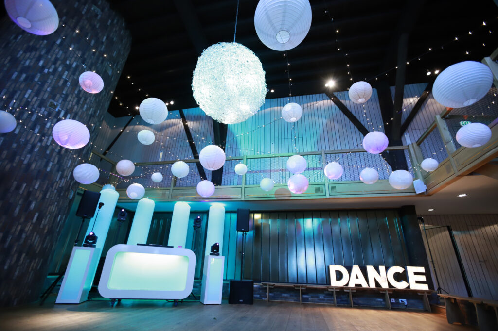 Feestzaal van de Pollepleats met witte DJ-booth, lichtbollen aan het plafond en een DANCE-lichtbord