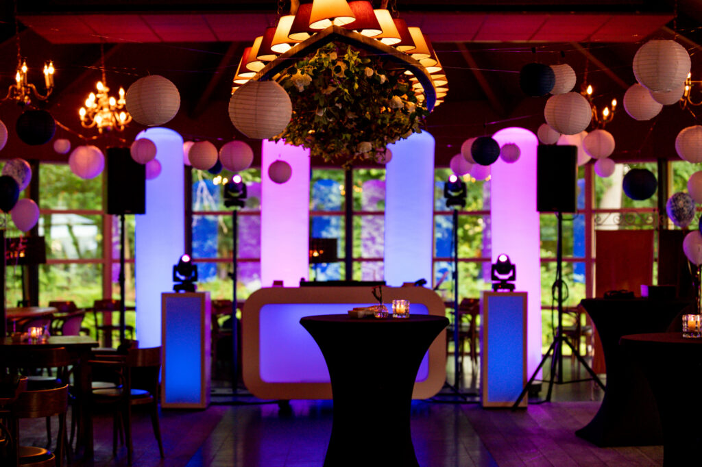 Feestzaal van Landgoed Stania State met verlichte DJ-booth, lichtzuilen en kroonluchters