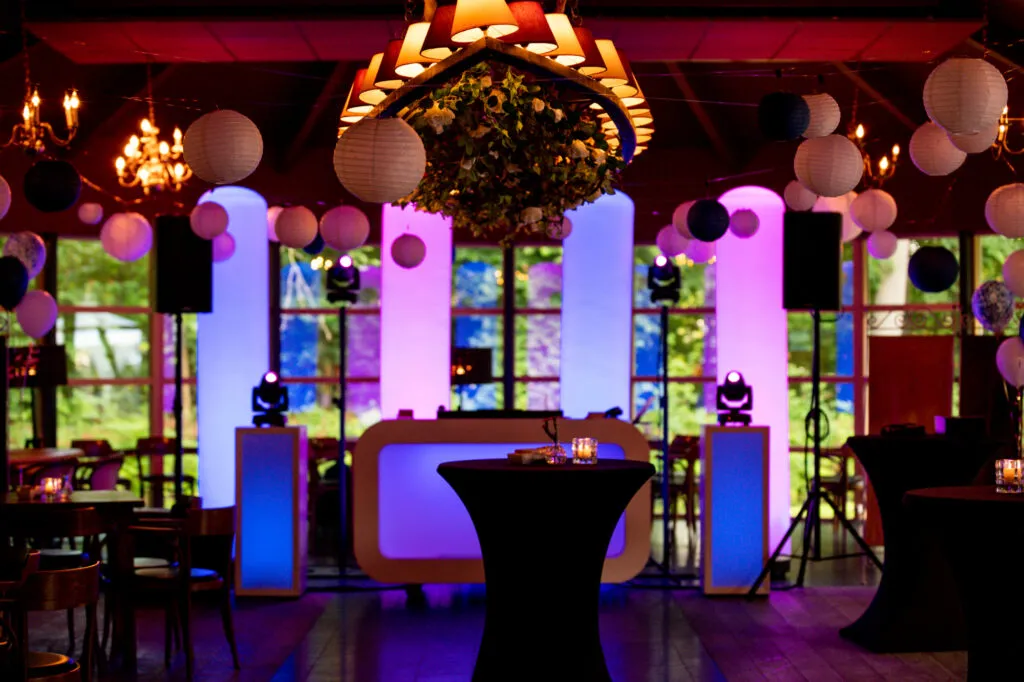 Feestzaal van Landgoed Stania State met verlichte DJ-booth, lichtzuilen en kroonluchters