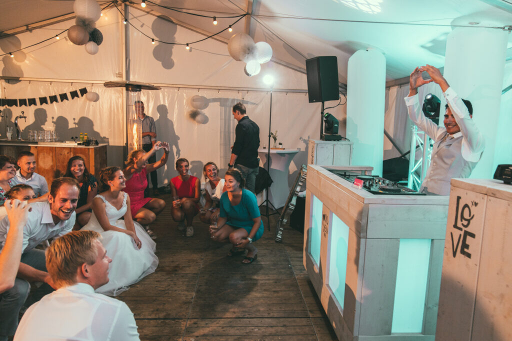 Steigerhouten DJ-booth met LOVE-opdruk in een feesttent, met gasten op de dansvloer