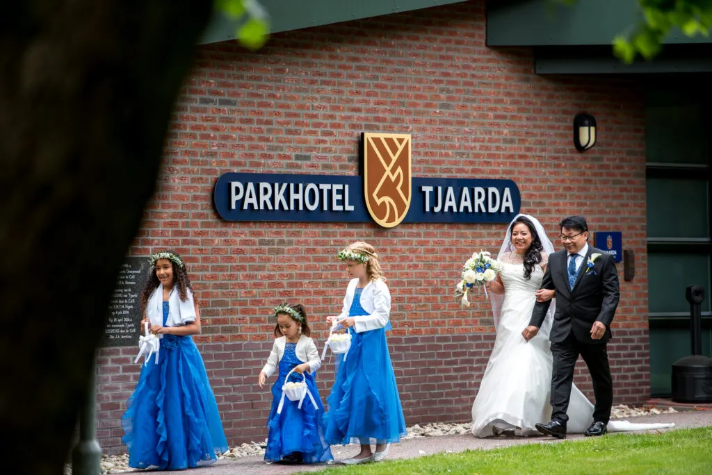 Bruidspaar met bruidsmeisjes in blauwe jurken voor de gevel van Parkhotel Tjaarda