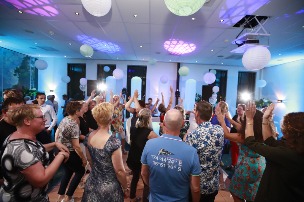 Volle dansvloer met gasten onder blauwe en paarse verlichting in Parkhotel Tjaarda
