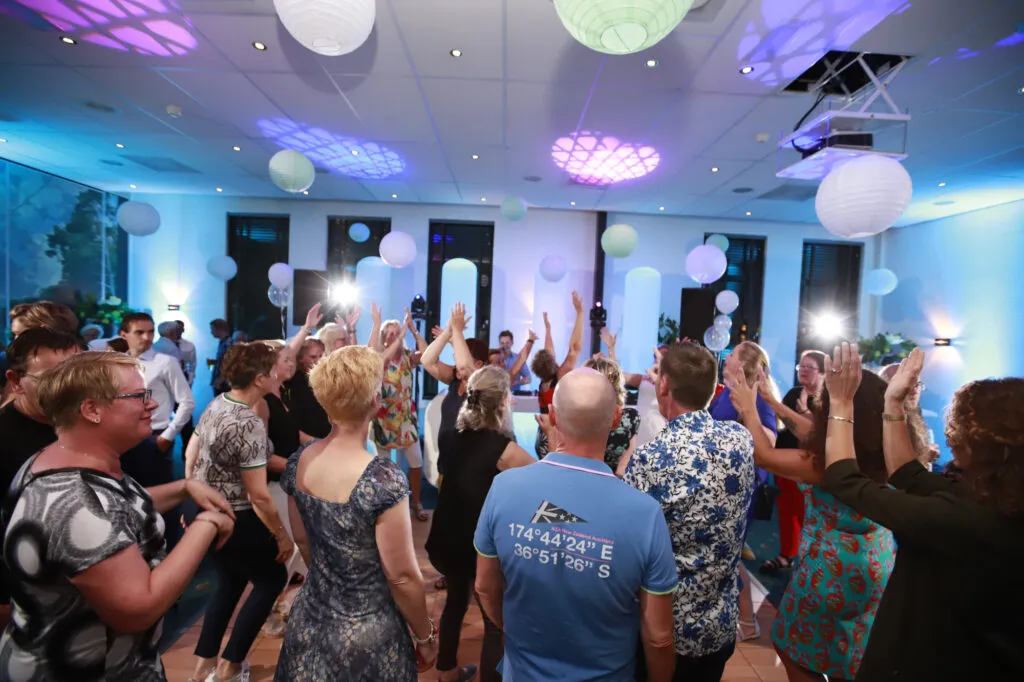 Volle dansvloer met gasten onder blauwe en paarse verlichting in Parkhotel Tjaarda