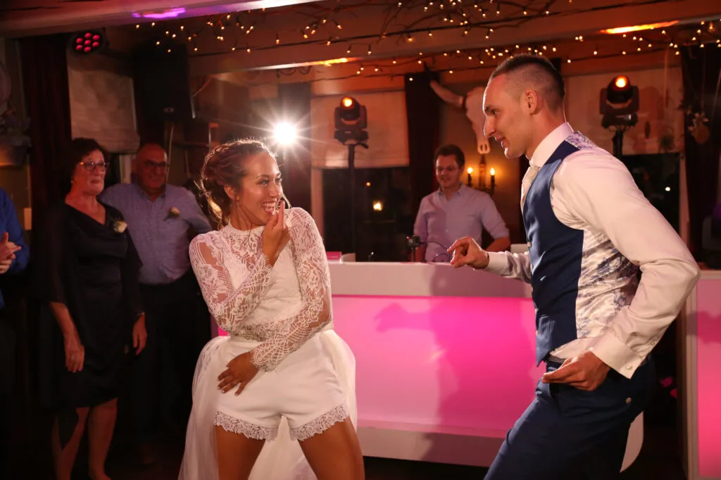 Bruidspaar lacht op de dansvloer voor de roze verlichte DJ-booth bij De Kruimel