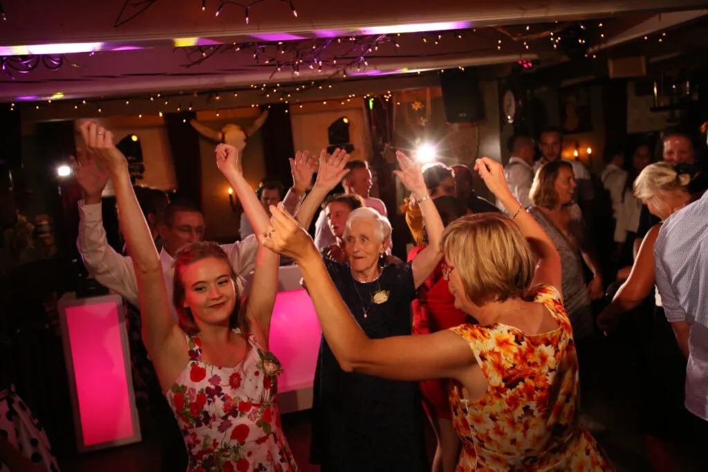 Gasten van alle leeftijden dansen met de handen in de lucht bij De Kruimel