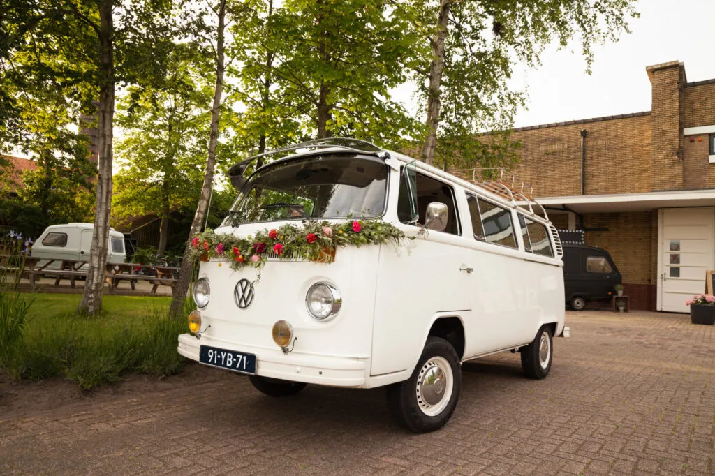 Een witte Volkswagen-bus met bloemen als trouwauto bij Lokaal 55